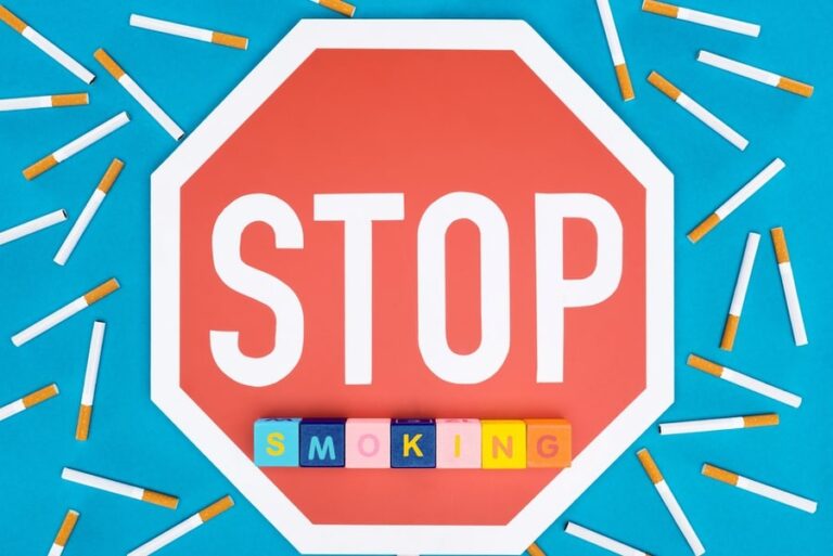 Top view of stop sign, cigarettes and blocks with letters isolated on blue, stop smoking concept